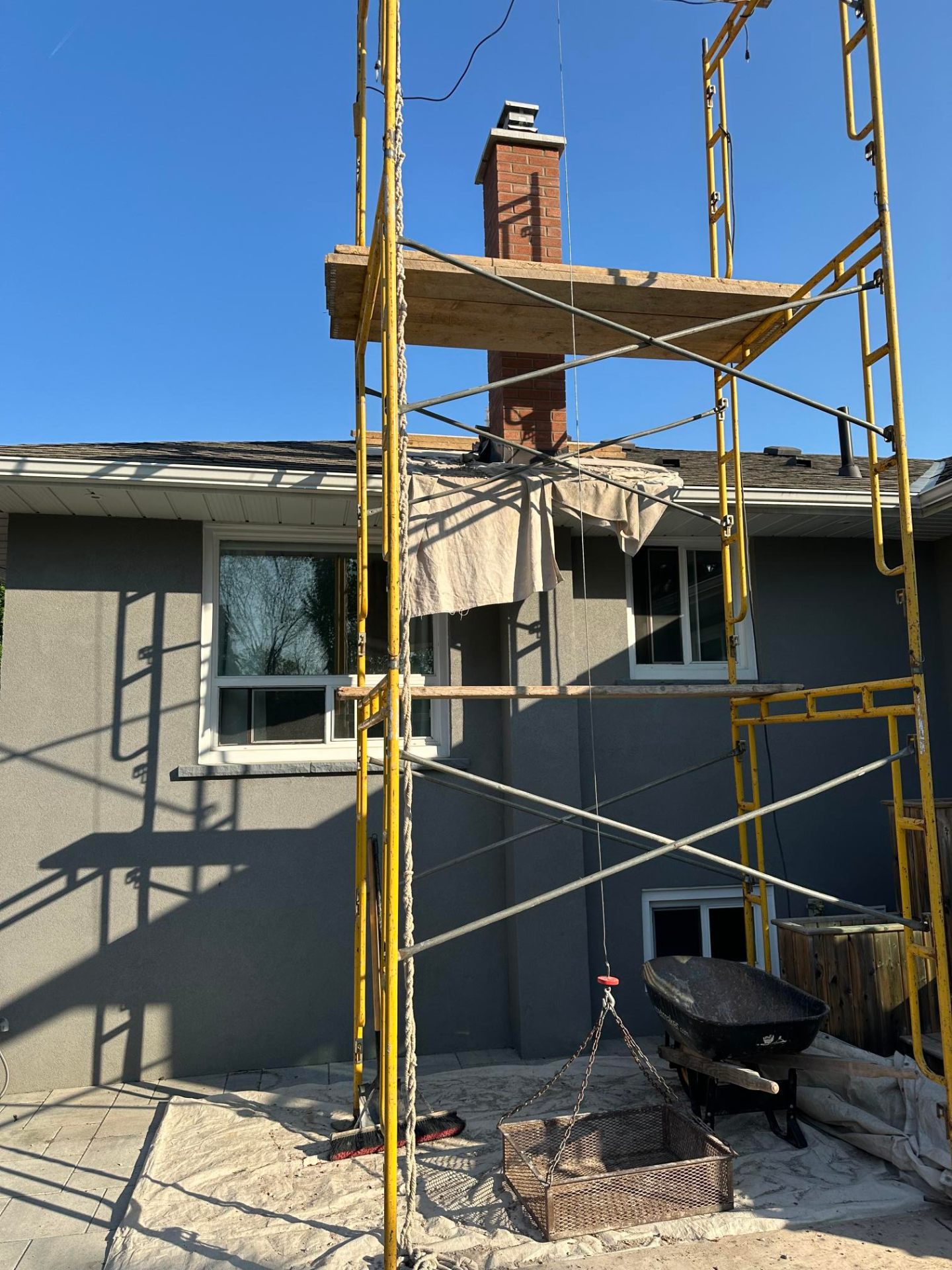 Freshly recoated grey stucco facade with restored brick chimney above